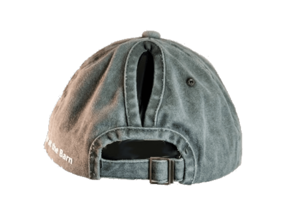 A washed gray-green baseball cap shown from the back, featuring a fabric strap with a metal buckle and white embroidered text reading 'at the Barn' on the side.