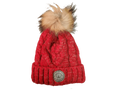 A red cable-knit beanie hat featuring a fluffy tan and brown faux-fur pom-pom on top and a circular leatherette equestrian lifestyle brand badge on the front cuff.