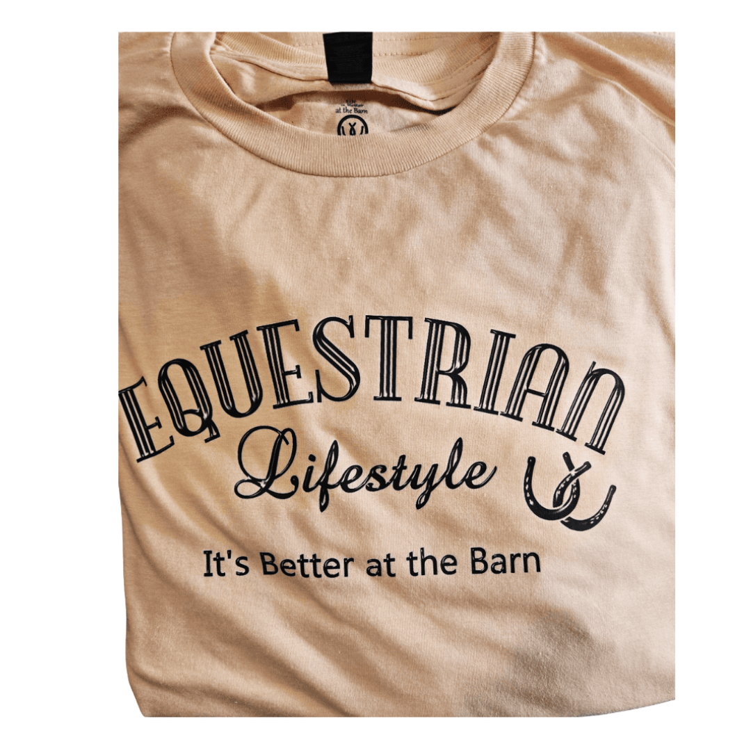 A beige t-shirt with a black graphic print that reads 'EQUESTRIAN Lifestyle It's Better at the Barn' along with a horseshoe illustration, shown on a plain white background.