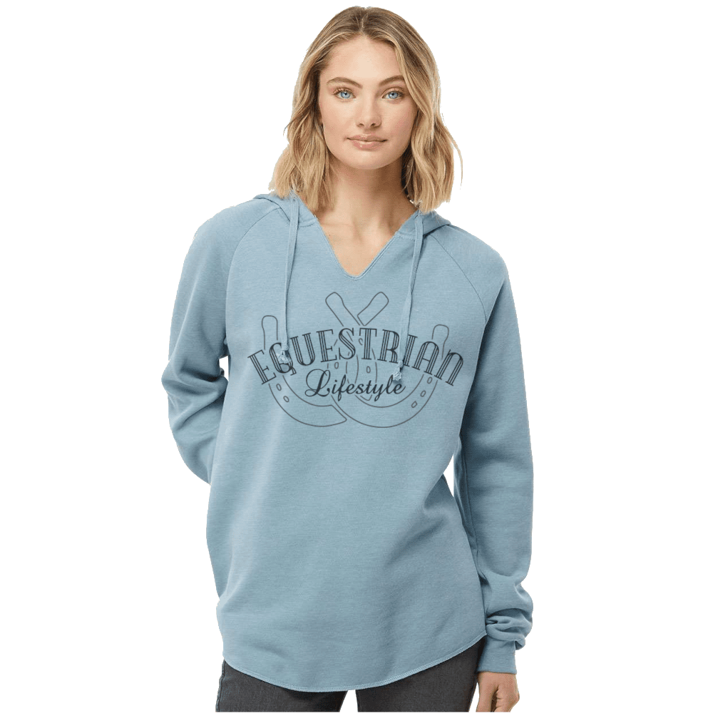 A woman wearing a light blue pullover hoodie with a dark gray graphic on the front that reads 'EQUESTRIAN Lifestyle' with a horseshoe  design, set against a plain white background.