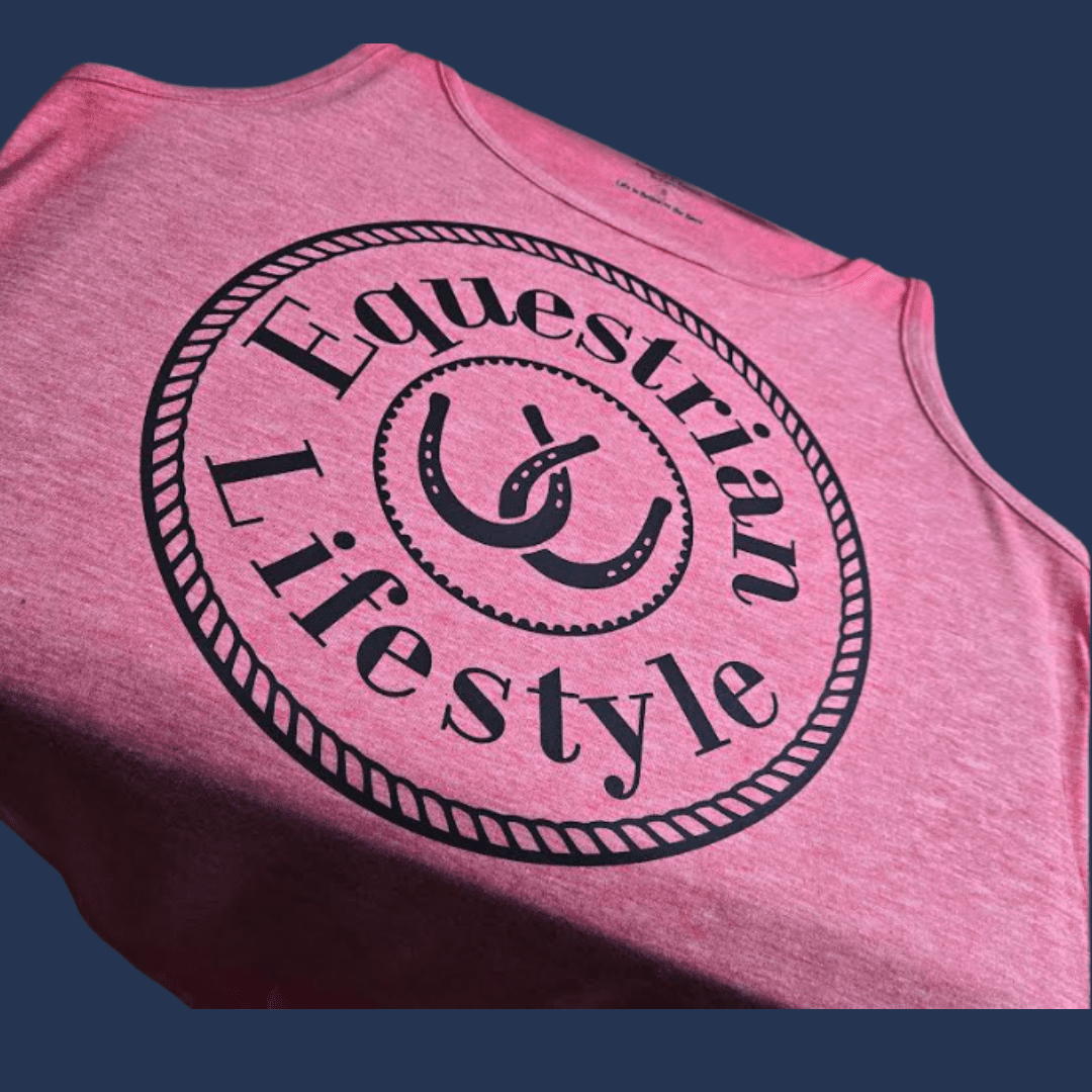 A close-up of a heather pink sleeveless tank top with a large black circular graphic reading 'Equestrian Lifestyle' and a horseshoe emblem, shown against a dark blue background.