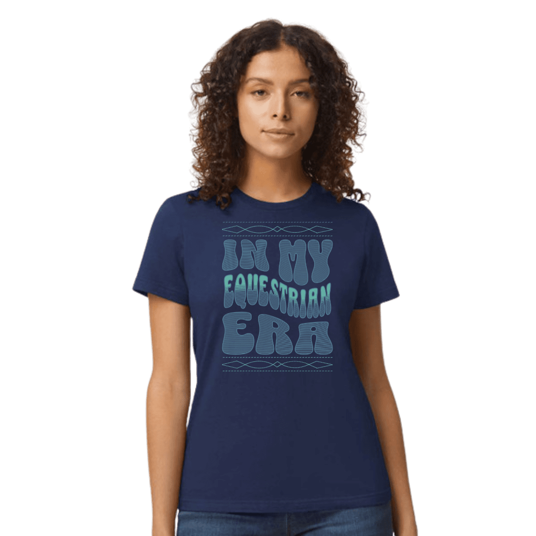 A woman with curly brown hair wearing a navy blue t-shirt with a light blue graphic text that reads 'IN MY EQUESTRIAN ERA'.