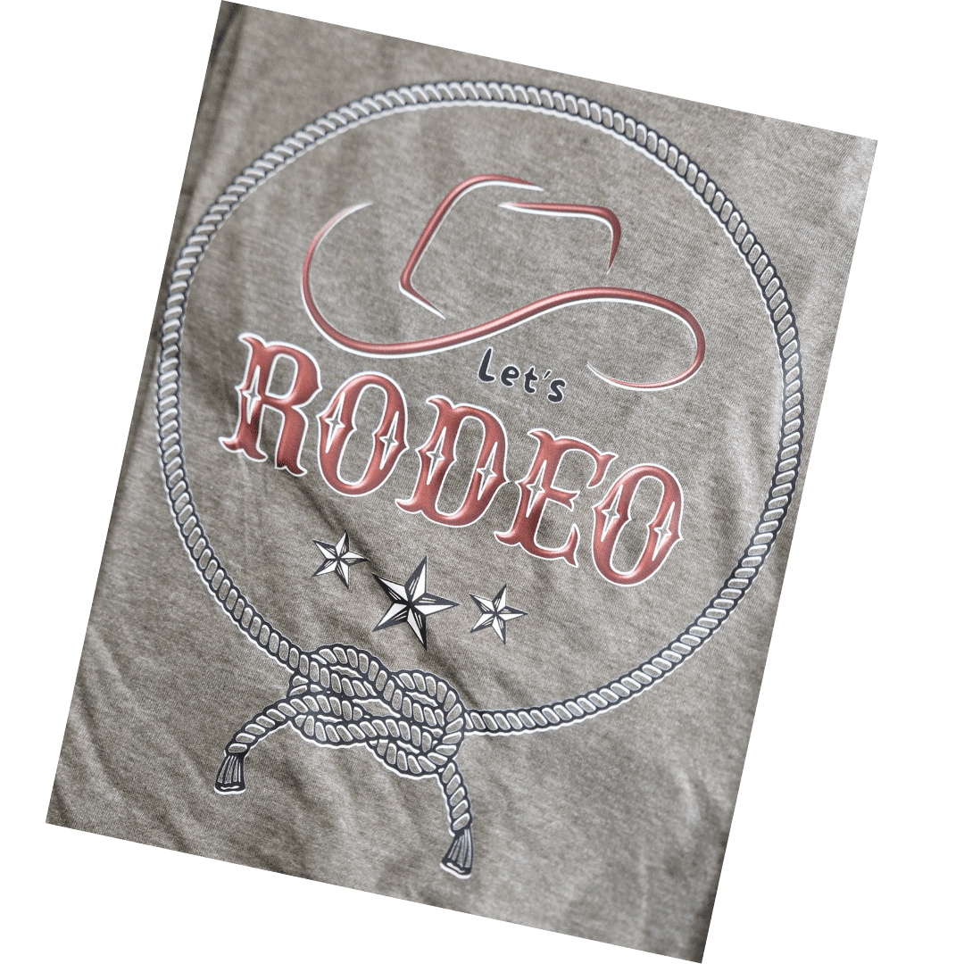 A close-up of a heather gray fabric surface featuring a western-themed graphic with the words 'Let's RODEO,' a cowboy hat outline, rope border, stars, and a tied lasso design.