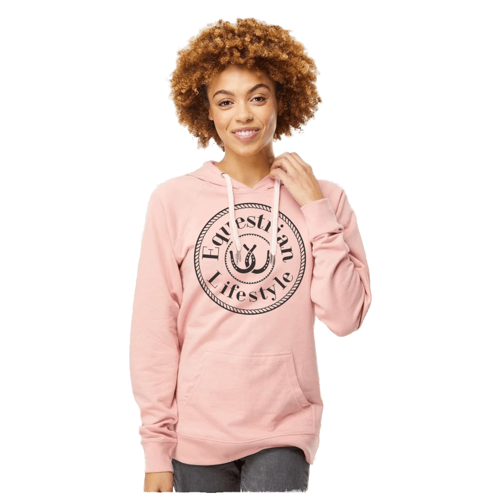A woman with curly light brown hair wearing a light pink pullover hoodie with a black circular graphic on the chest that reads 'Equestrian Lifestyle'. She is standing against a solid white background.
