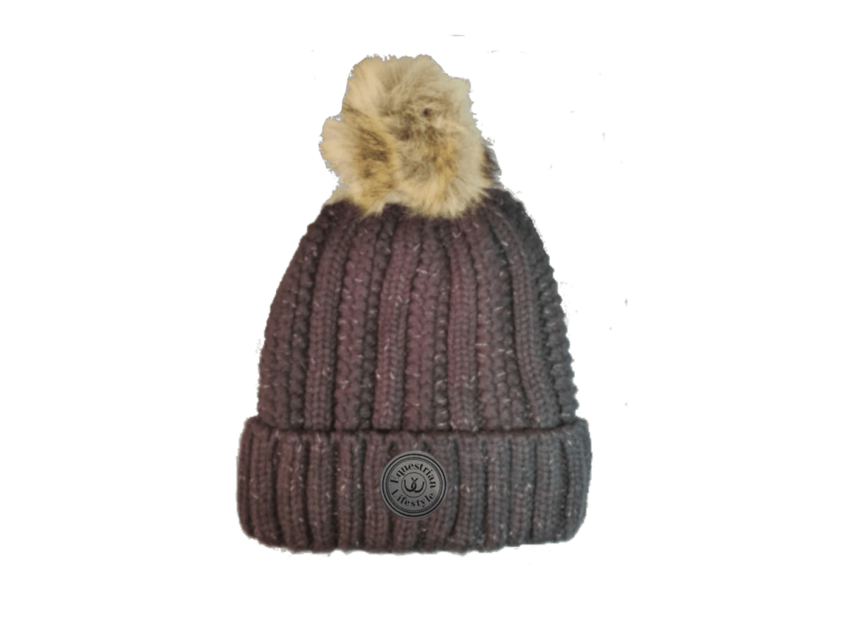 A ribbed knit beanie hat in a dark plum-brown color with a fluffy beige faux-fur pom-pom on top and a circular leatherette equestrian lifestyle  brand patch on the front cuff.