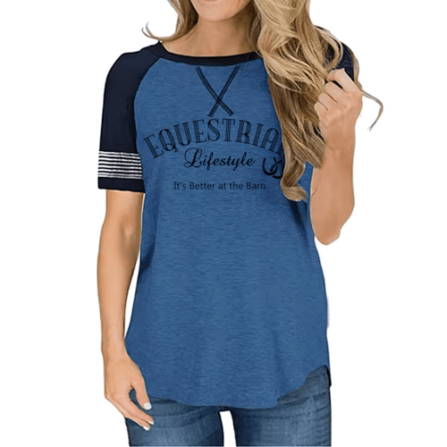 A woman wearing a heather blue raglan t-shirt with navy sleeves and a graphic print that reads 'EQUESTRIAL Lifestyle' and 'It's Better at the Barn'.