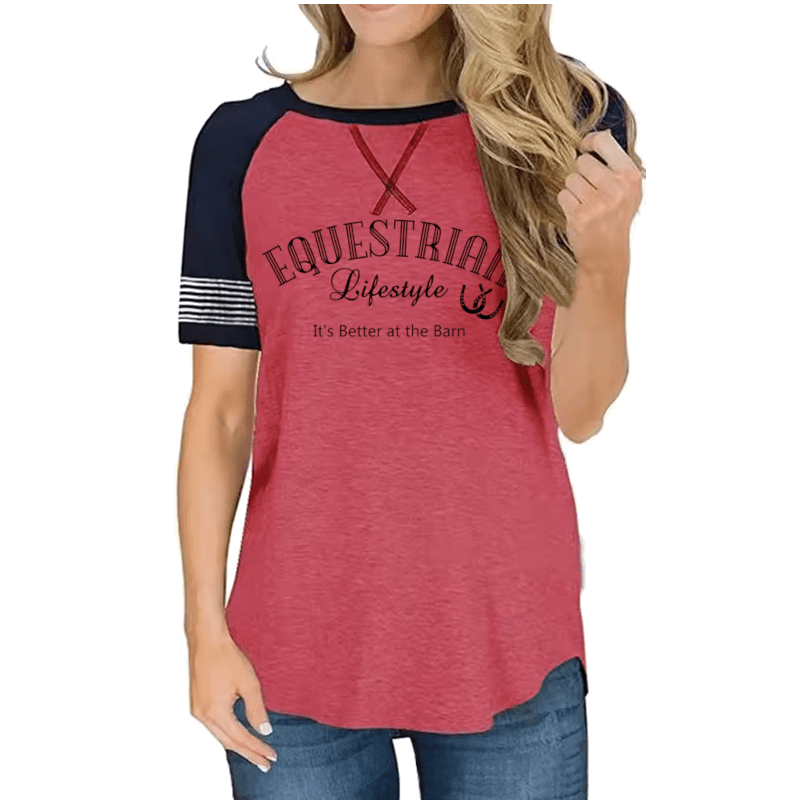 A woman wearing a heathered coral pink raglan t-shirt with navy blue sleeves and a graphic print that reads 'EQUESTRIAL Lifestyle & It's Better at the Barn'.