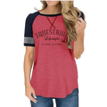 A woman wearing a heathered coral pink raglan t-shirt with navy blue sleeves and a graphic print that reads 'EQUESTRIAL Lifestyle & It's Better at the Barn'.