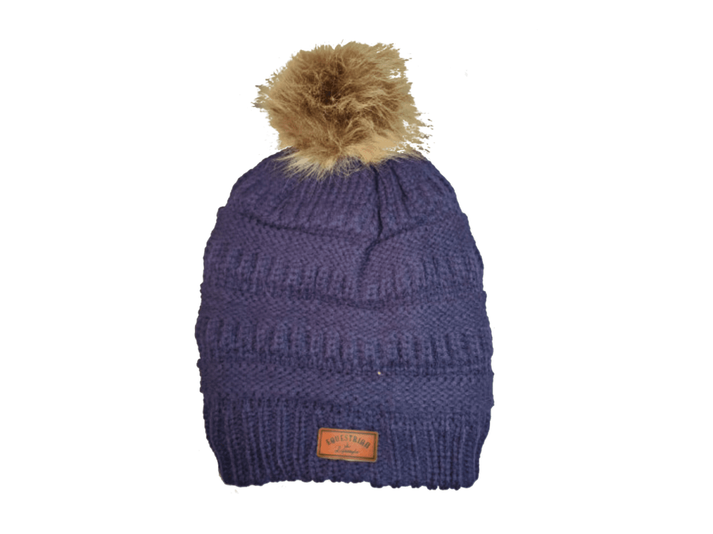 A ribbed knit beanie hat in a dark purple color, featuring a fluffy tan faux-fur pom-pom on top and a small brown leatherette equestrian lifestyle brand patch near the bottom cuff.