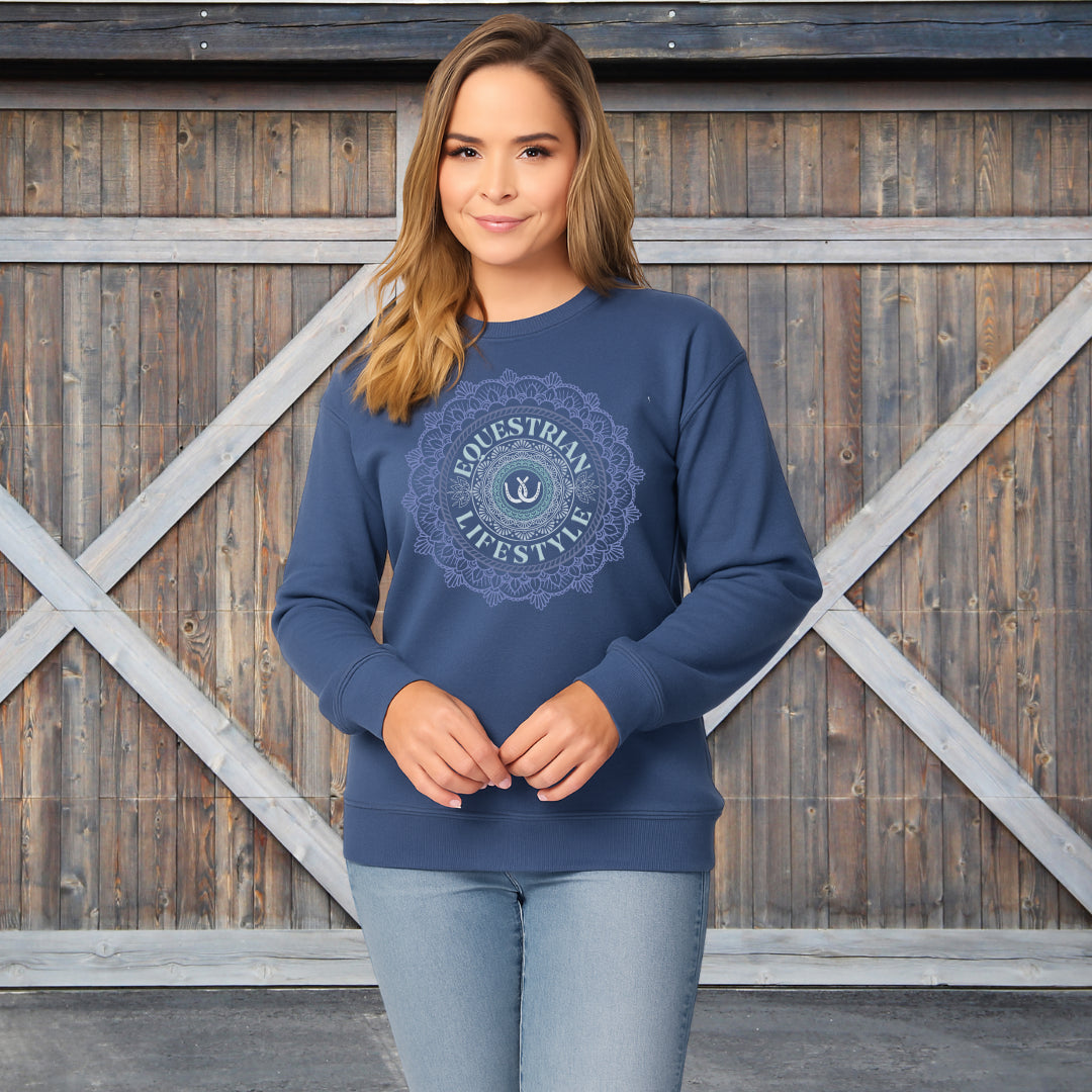 A woman modeling a navy blue crewneck sweatshirt with a circular 'Equestrian Lifestyle' graphic on the chest, standing in front of a rustic wooden barn door.