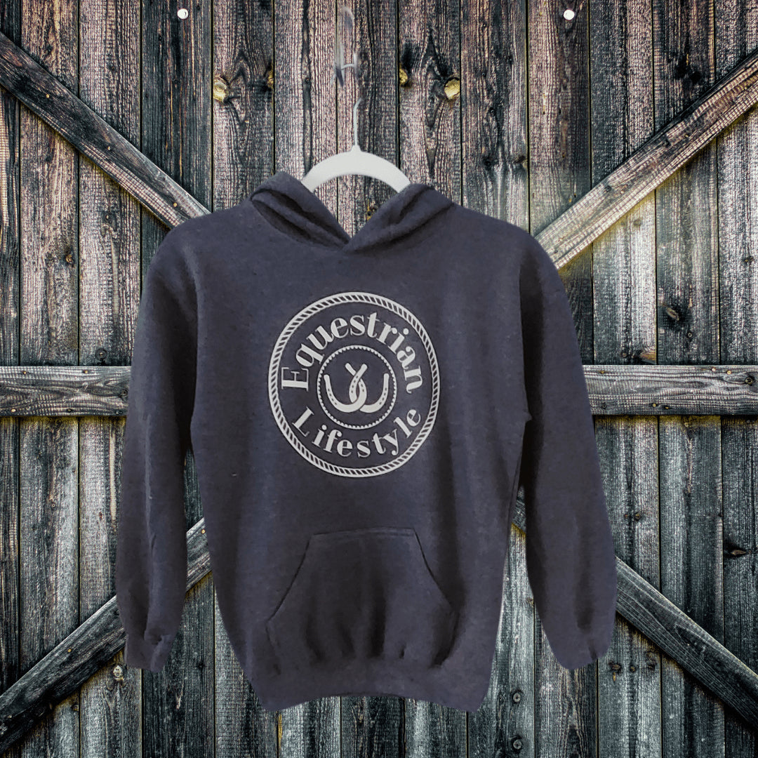 A dark charcoal gray hoodie with a white circular graphic reading 'Equestrian Lifestyle' hanging on a white plastic hanger against a rustic wooden barn door background.